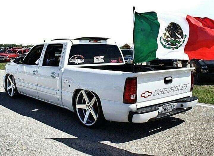 White Chevrolet pick-up truck with a large Mexican flag waving from the rear truck bed.
