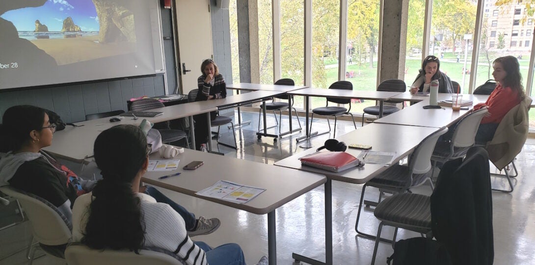 Instructor and students at a class meeting in GH 207. Desks are arranged in a ring, instructor and students are carrying on a discussion.