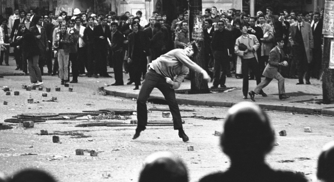 student throwing rock while crowds watch